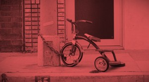A tricycle chained to the side of a building.