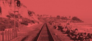 A red photo of the train tracks in front of some rocks.