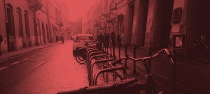 A red photo of a street with parked cars and bicycles.